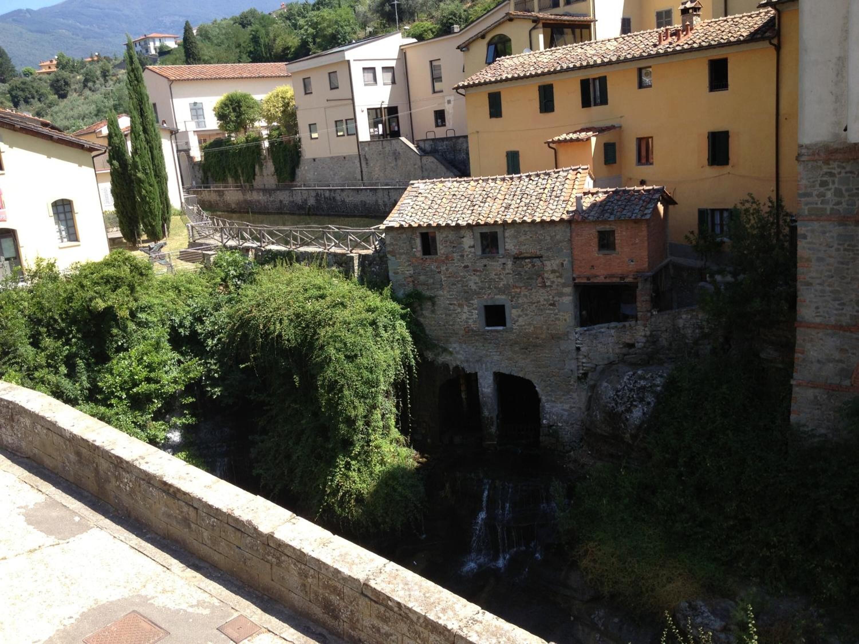 A stone bridge over a river, surrounded by buildings with tiled roofs and greenery.