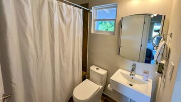 A bathroom with a shower curtain, toilet, sink, and a window above the sink.
