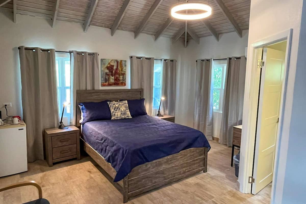 A bedroom with a wooden bed, a nightstand, a desk, and a small refrigerator.