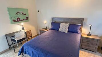 Quarto com uma cama grande, duas mesas de cabeceira com luminárias, uma cadeira e uma obra de arte na parede.