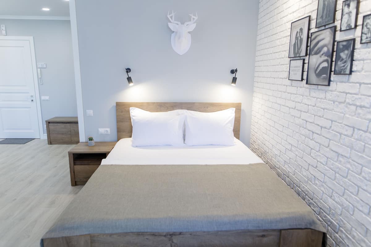 Un dormitorio moderno con cabecera de madera, ropa de cama blanca y una pared de ladrillo con cuadros enmarcados.