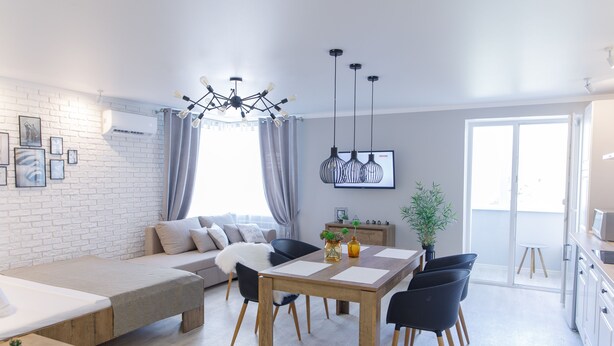 A modern living space with a sofa, dining table, and chairs, a kitchen area, and a large window providing natural light. - Royal Suite near Lake (Sumy)