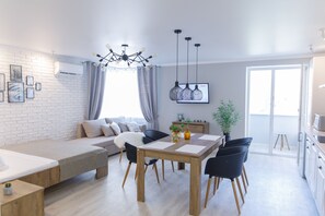 A modern living space with a sofa, dining table, and chairs, a kitchen area, and a large window providing natural light. - Royal Suite near Lake (Sumy)