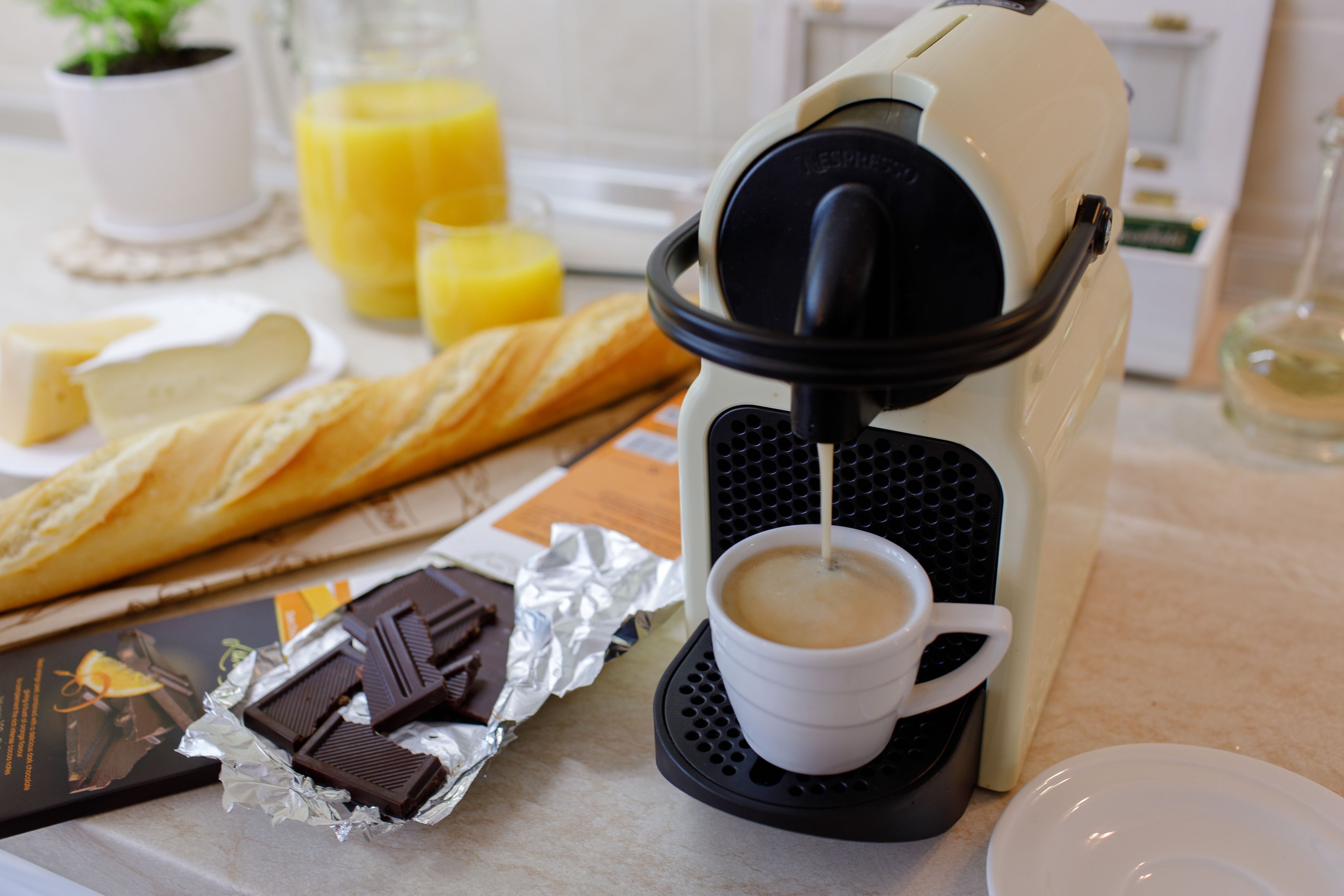 A coffee machine dispensing coffee into a cup, with a croissant, chocolate pieces, and a chocolate bar on the table.