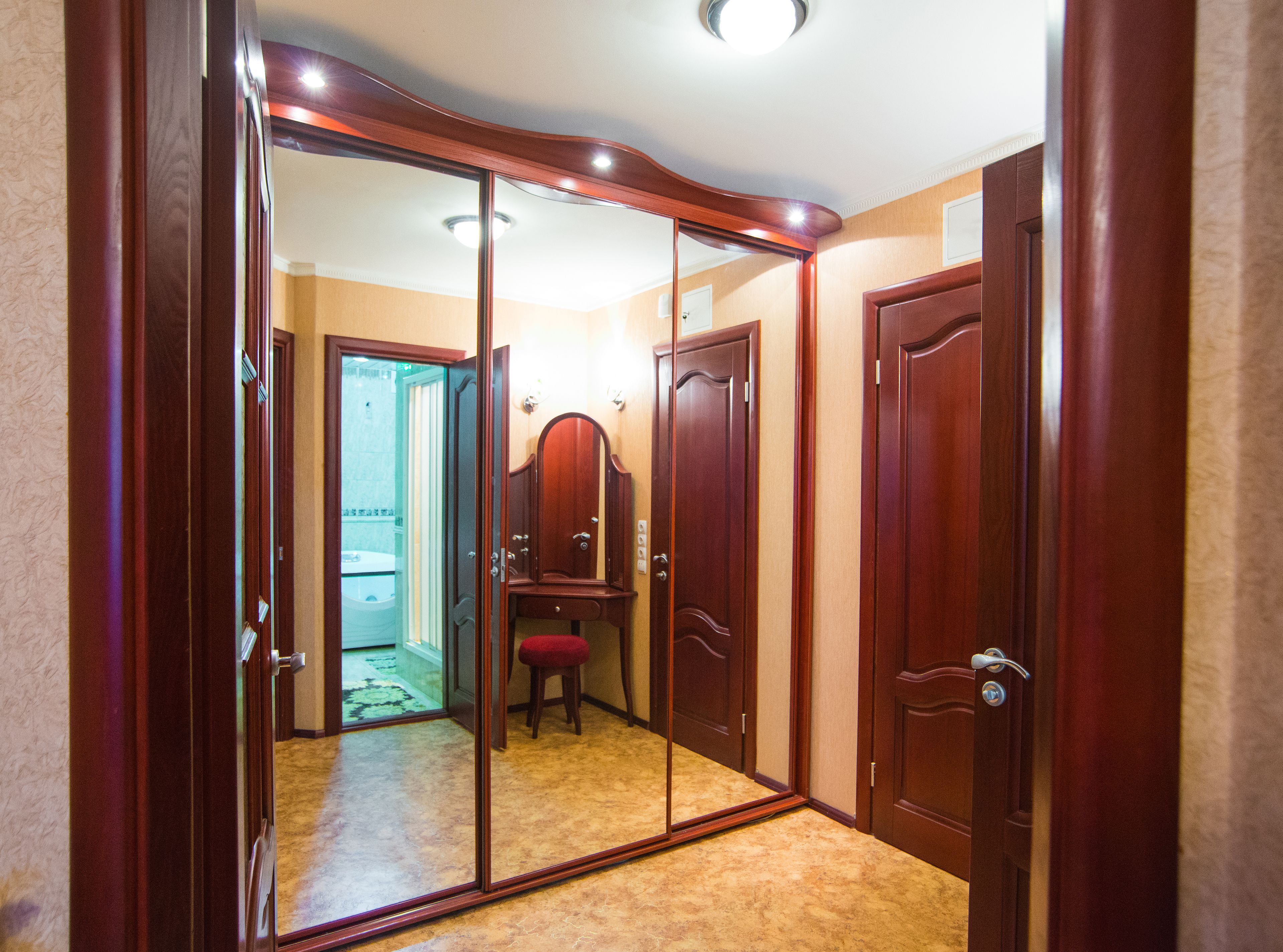 Une pièce avec un grand miroir, une armoire en bois et un petit tabouret.