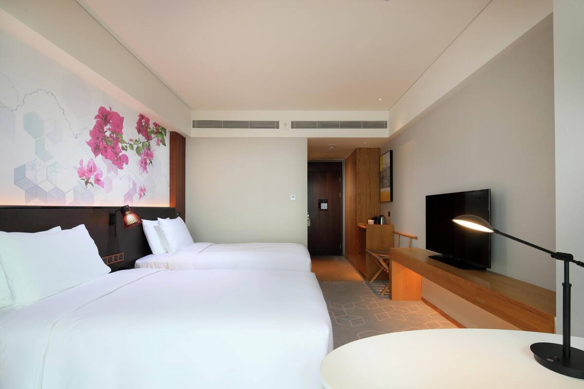 Ein Hotelzimmer mit zwei Betten, einem Fernseher, einem Schreibtisch und einer Wandlampe.