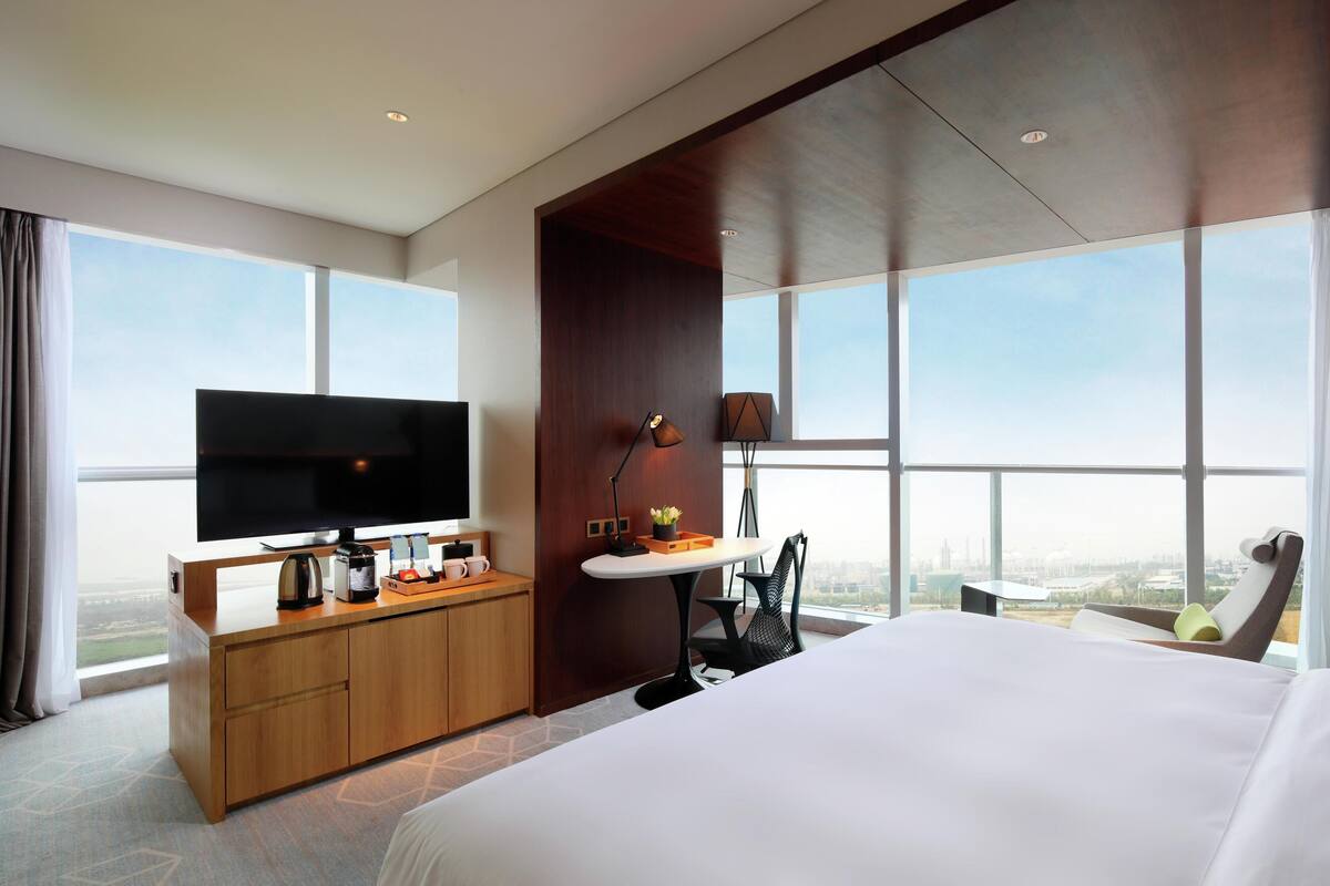 Ein modernes Hotelzimmer mit einem großen Bett, einem Flachbildfernseher, einem Holztisch und Blick auf die Stadt.