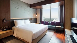 A modern hotel room with a large bed, a seating area with cushions, a small table, a TV, and a city view through the window. - Hilton Garden Inn Zhuhai Hengqin (Zhuhai)