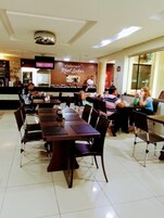 Un restaurante con una barra larga y varias mesas, un televisor montado en la pared y un suelo de baldosas.