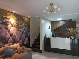 Zona de recepción con mostrador, escalera y pared con textura rocosa.