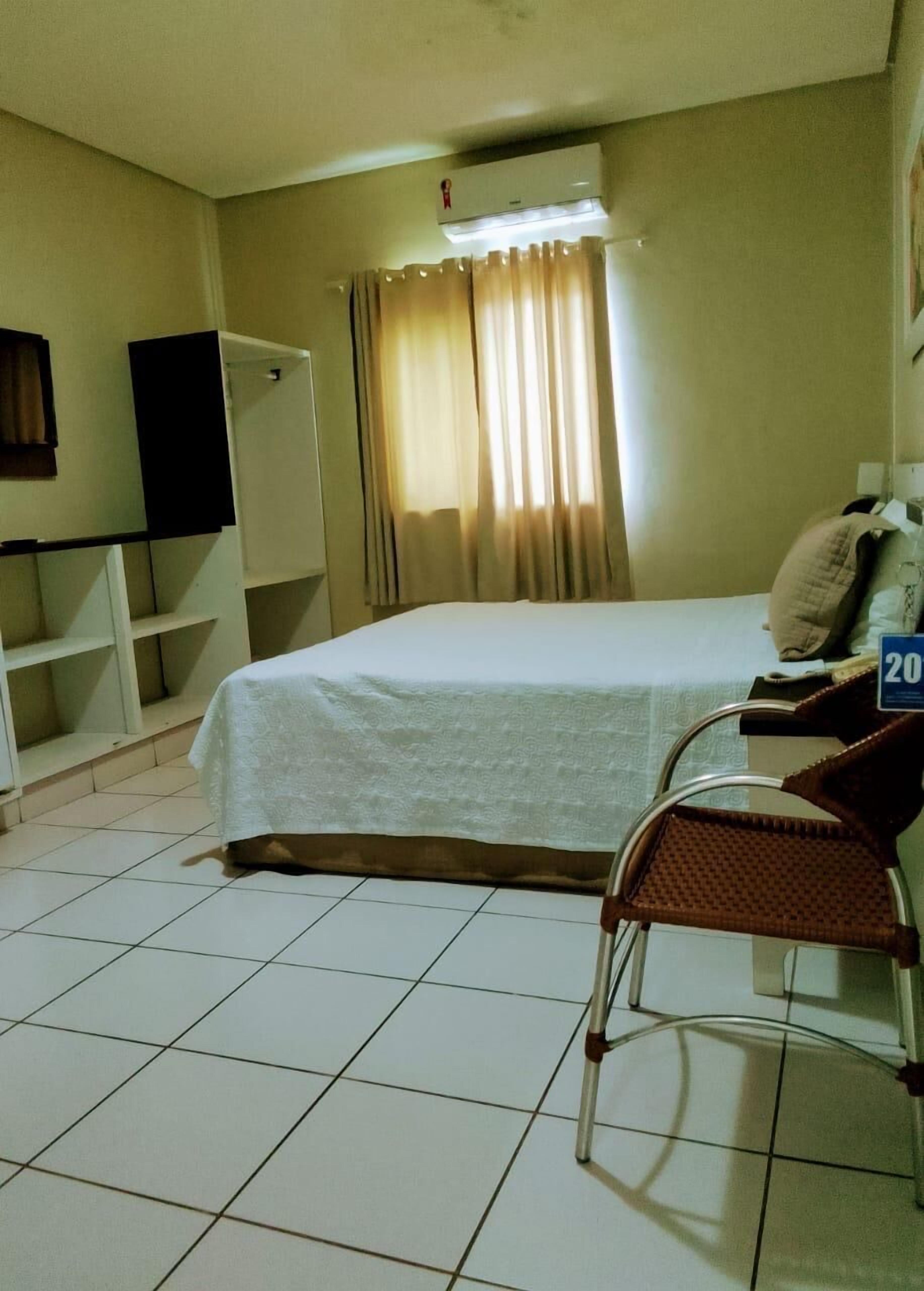 A hotel room with a bed, a chair, a wardrobe, and a television.