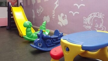 A children's play area with a yellow slide, green and blue toy cars, and a blue table.