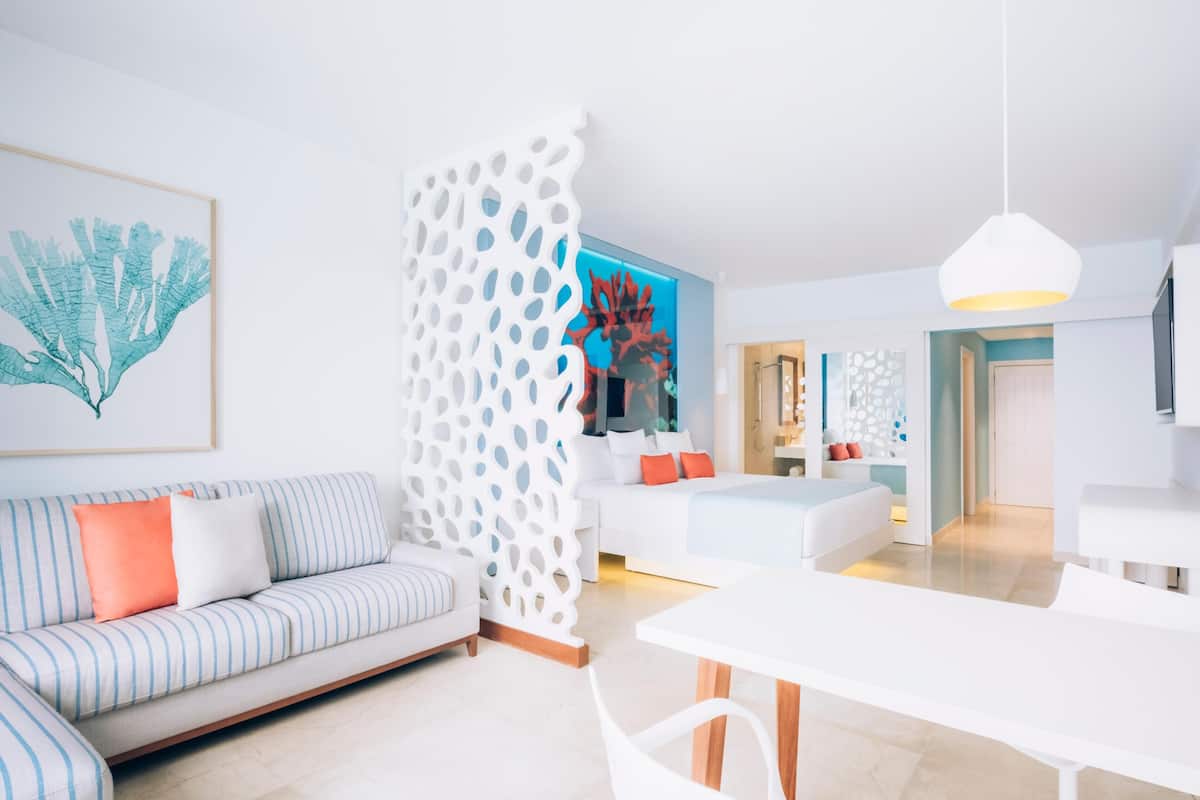 A modern living room with a sofa, a dining table, and a white partition with a geometric pattern.