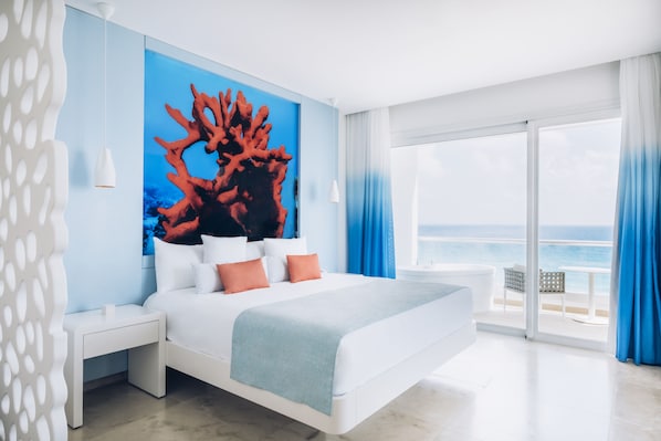 A modern hotel room with a large bed, a view of the ocean, and a tropical-themed wall mural.