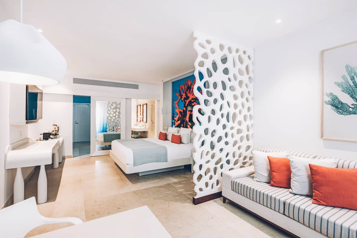A modern hotel room with a bed, a sofa, a desk, and a decorative wall.