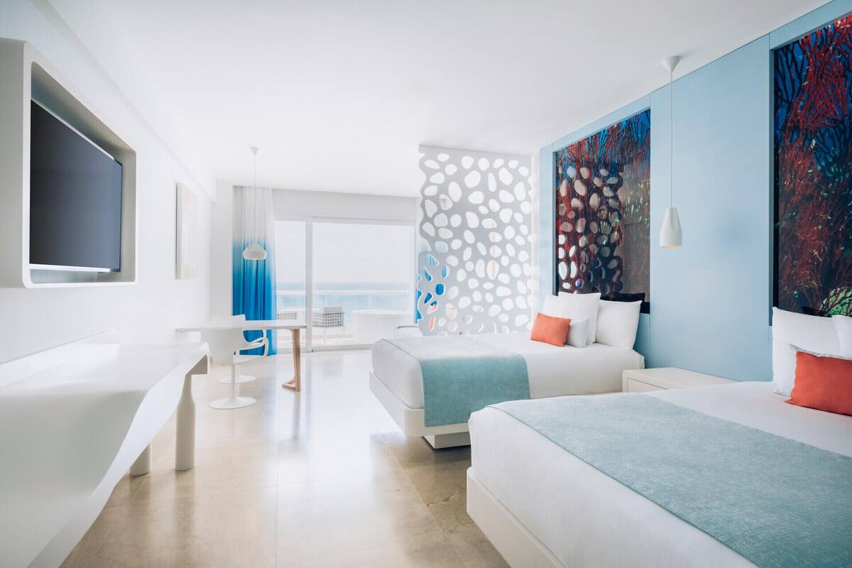 A modern hotel room with a large bed, a smaller bed, a desk, and a TV.