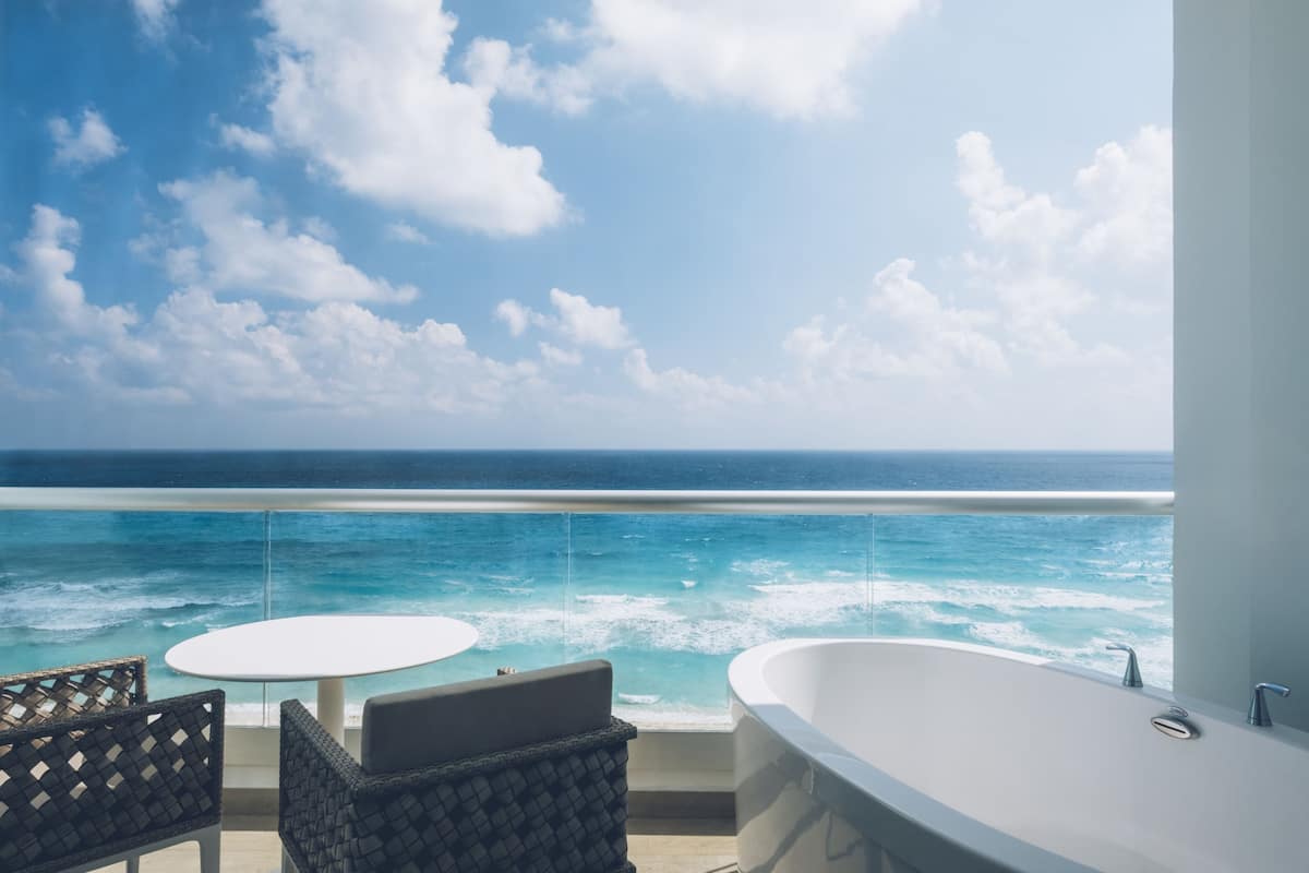 A balcony with a view of the ocean, a round table, and a bathtub.