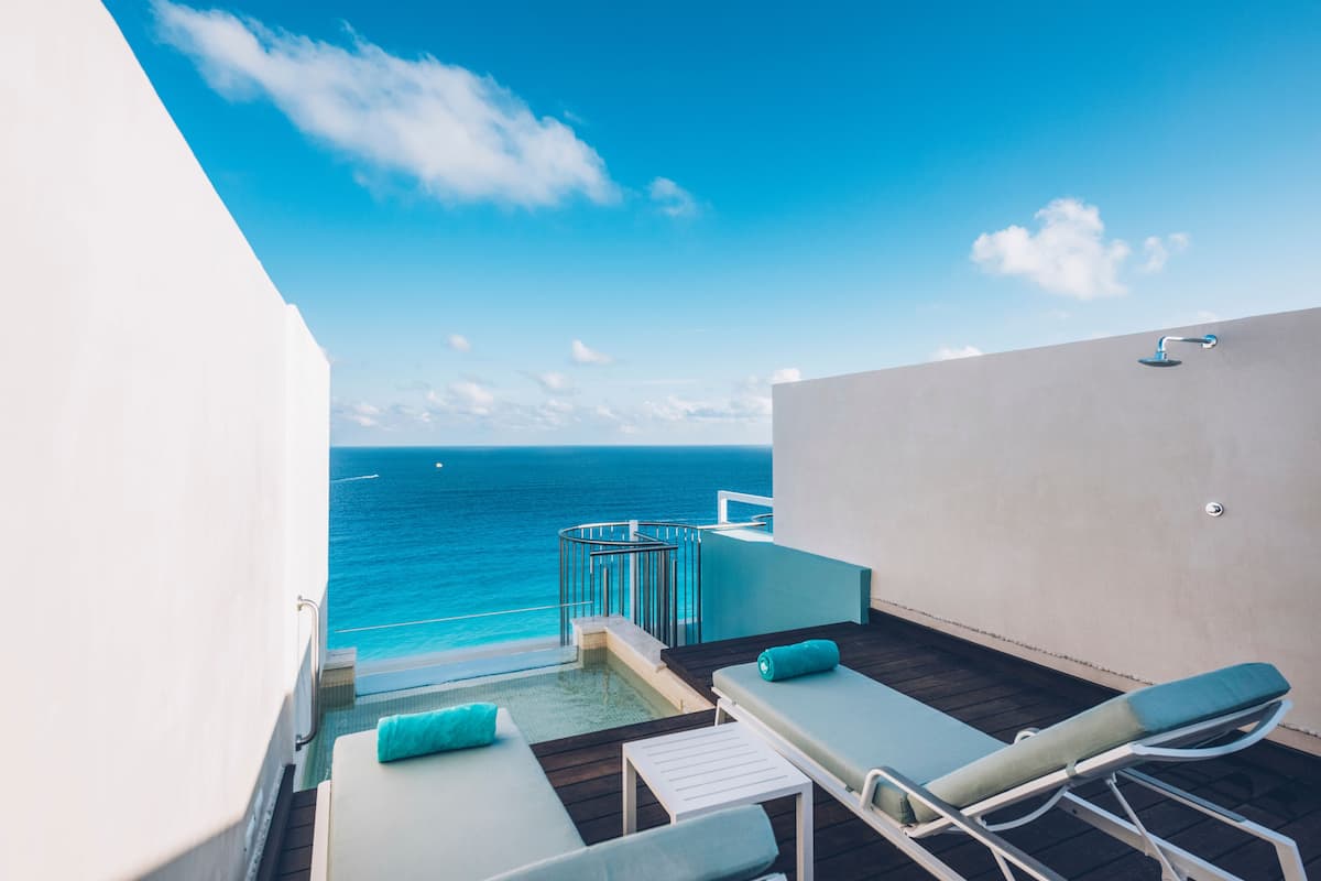 A balcony with a pool, lounge chairs, and a view of the ocean.