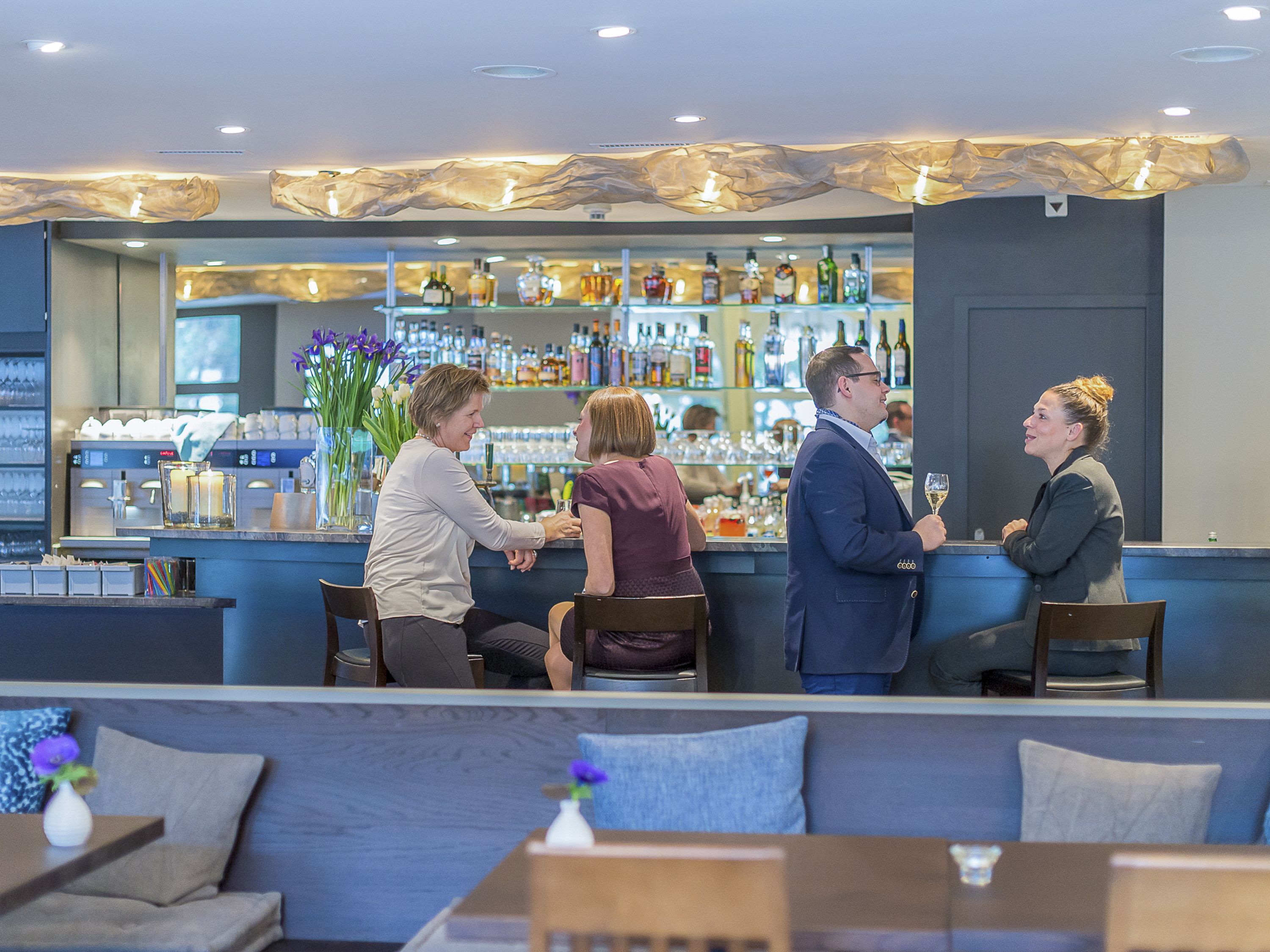 A bar area with a counter, seating, and a variety of bottles and glasses.