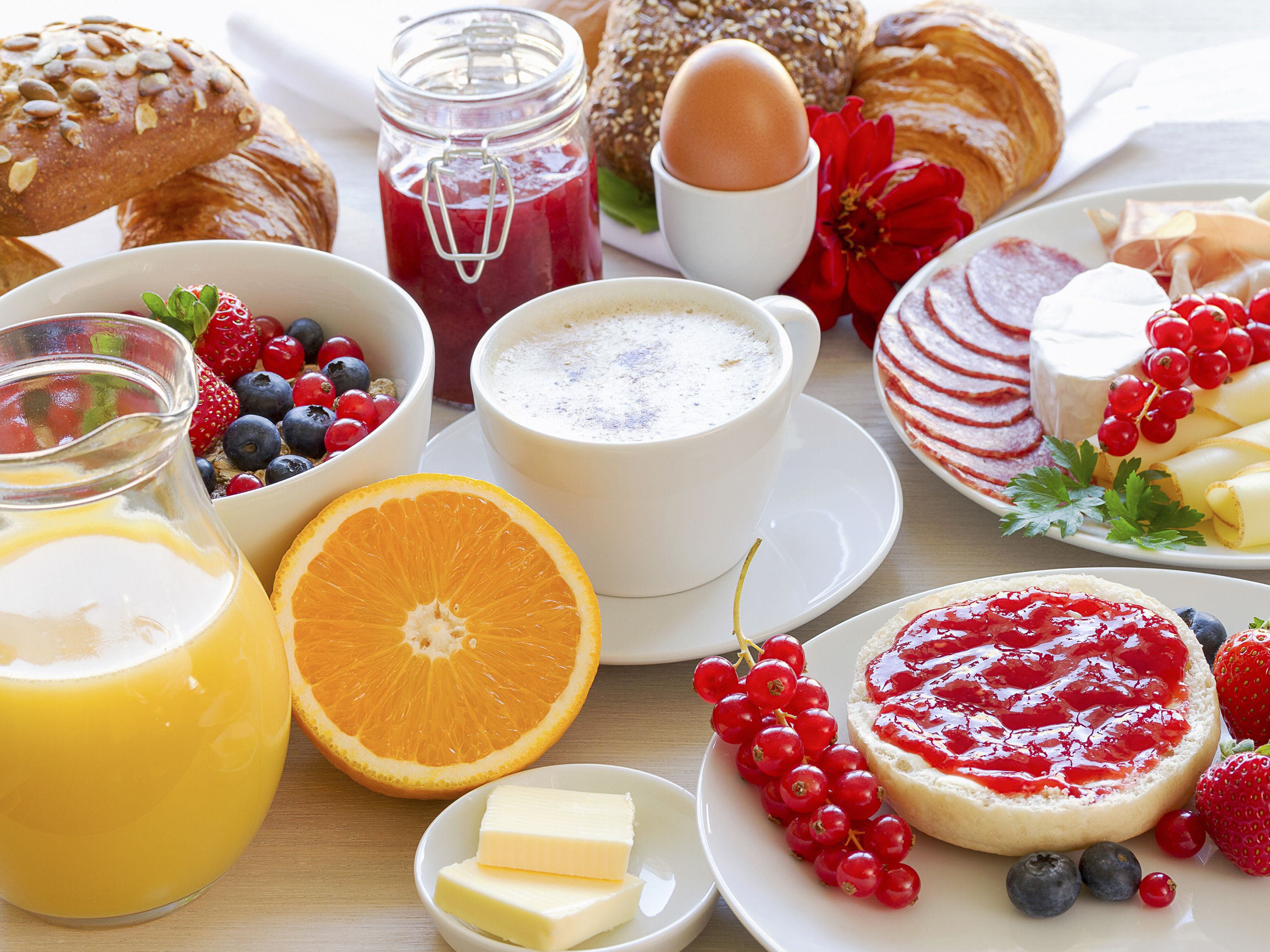 A breakfast table with various foods including bread, eggs, berries, and a glass of orange juice.
