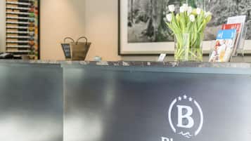 Un comptoir d’accueil orné d’un logo, d’un tableau encadré et d’un vase contenant des fleurs blanches.