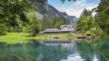 Un hôtel situé au bord d’un lac, avec un grand bâtiment, un quai avec des bateaux et une chaîne de montagnes en arrière-plan.
