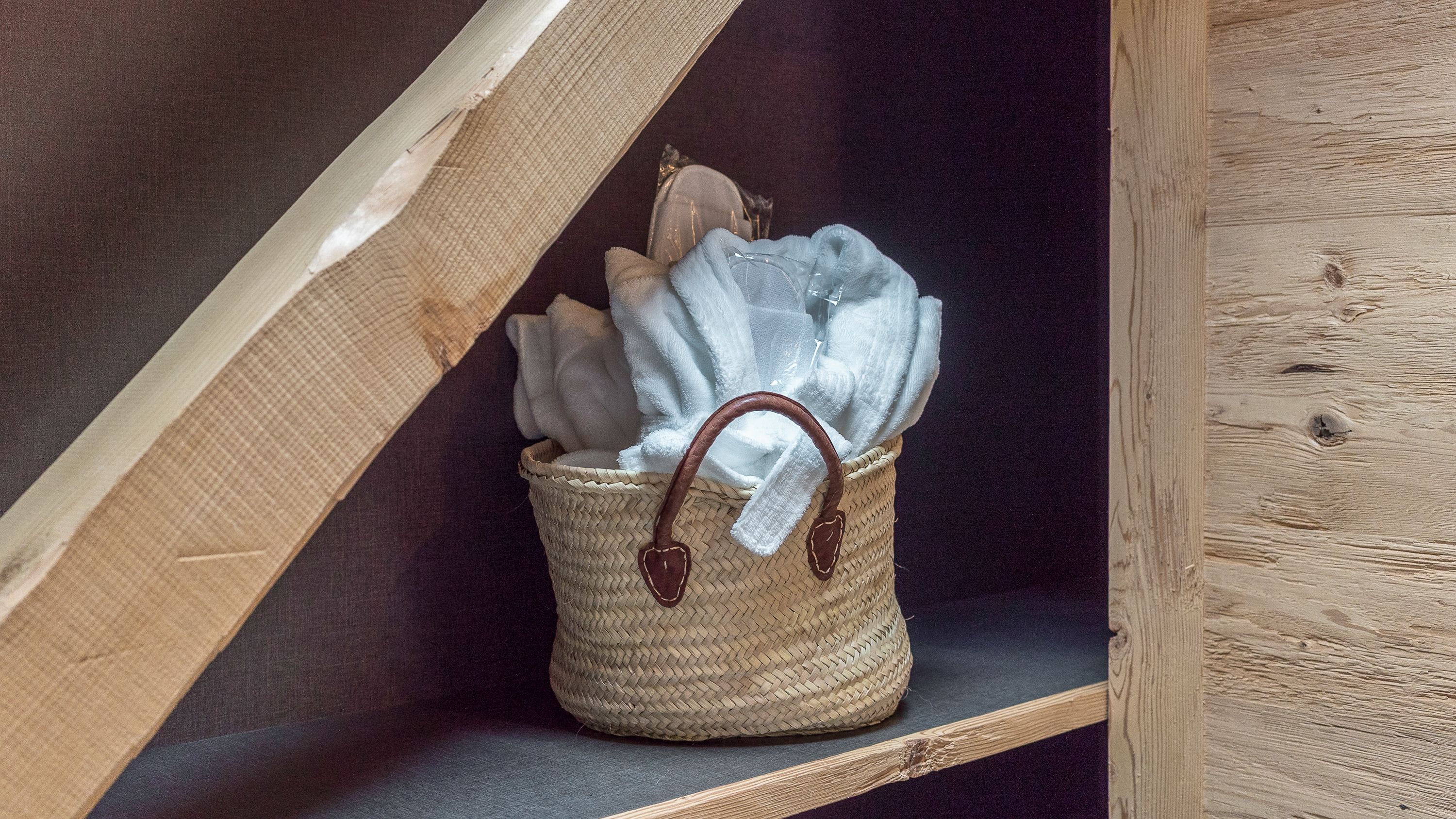 A woven basket with a handle, containing folded towels, placed on a shelf.