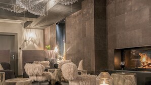 A modern lounge area with a fireplace, plush seating, and a decorative chandelier. - Hotel Blausee (Kandergrund)
