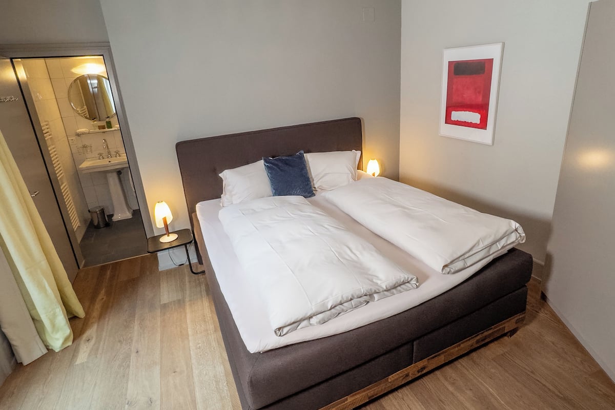 Una cama bien tendida con sábanas blancas, un cabecero de madera y dos lámparas de noche.