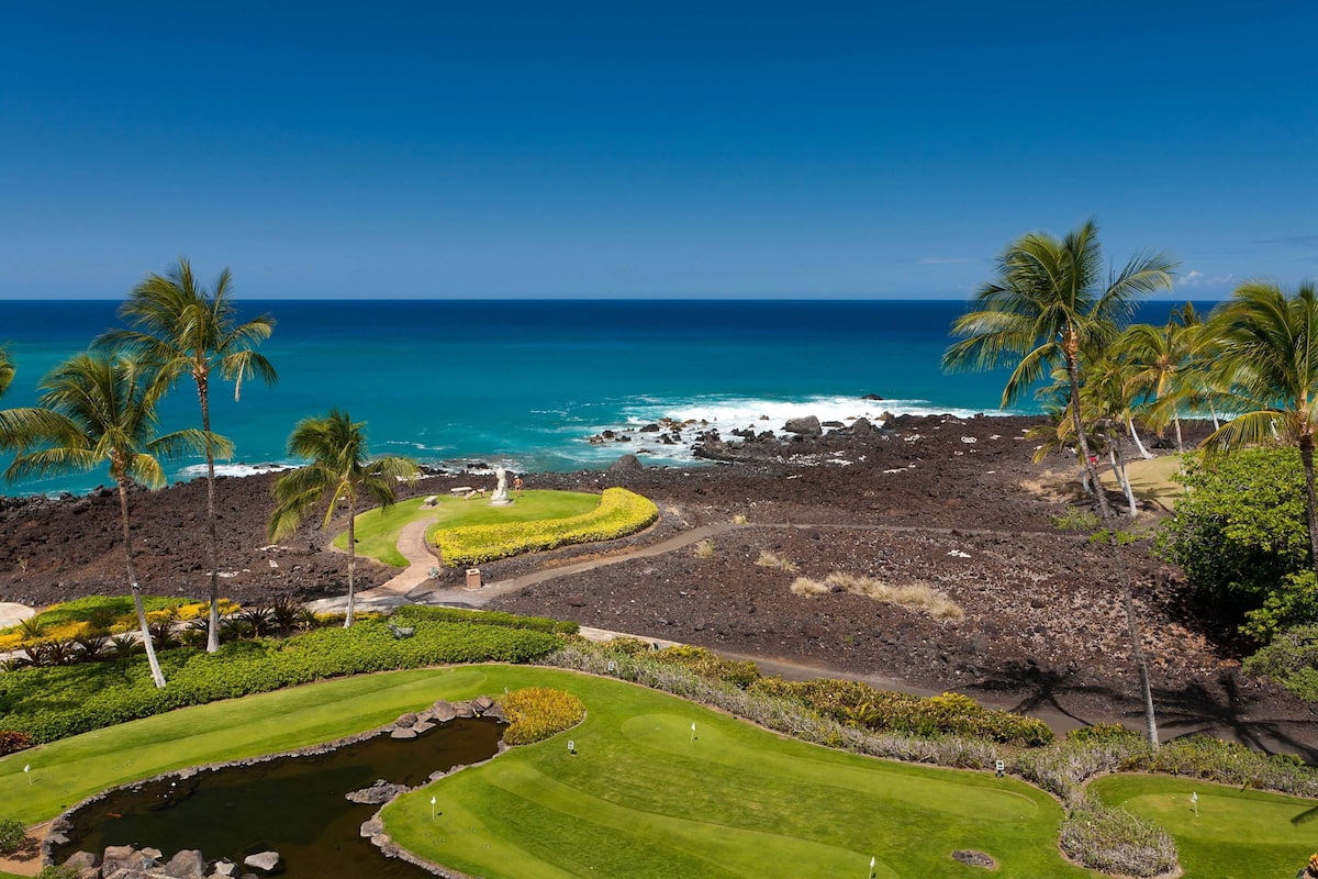 Un parcours de golf offrant une vue sur l’océan et les roches volcaniques.