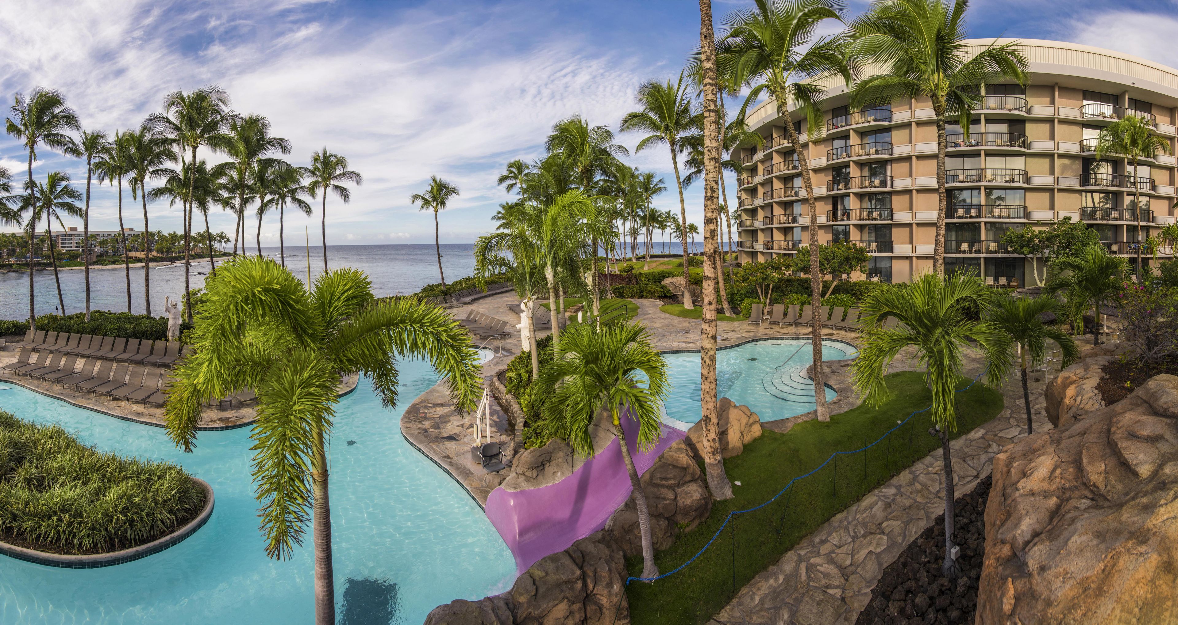 Um resort com várias piscinas, palmeiras e vista para o oceano.