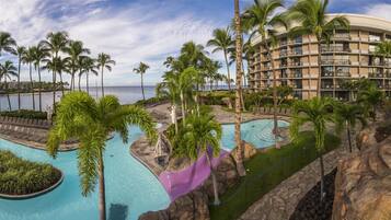 A resort with multiple swimming pools, palm trees, and a view of the ocean.