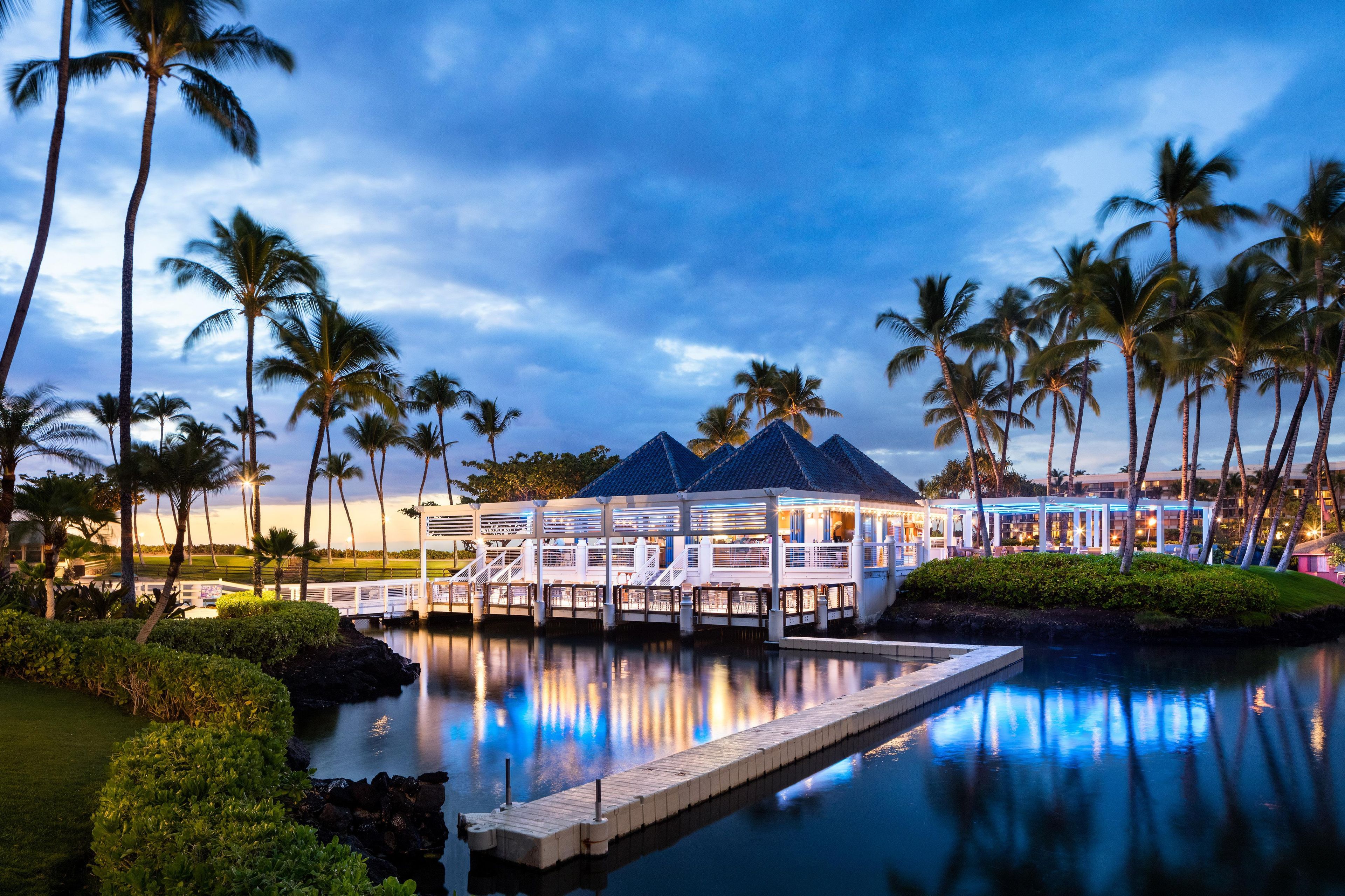 A resort with a pool, palm trees, and a covered area with seating.