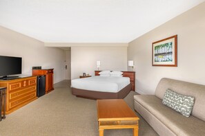 A hotel room with a bed, a television, a desk with a computer, a sofa, and a painting on the wall. - Hilton Grand Vacations Club Ocean Tower Waikoloa Village (Waikoloa)