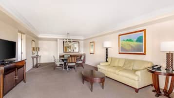 A hotel room with a TV, dining table, chairs, sofa, and a painting on the wall.