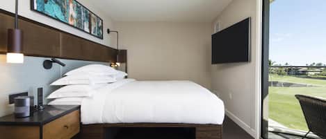 A modern hotel room with a large bed, a desk with a lamp, a flat-screen TV, and a view of a golf course.