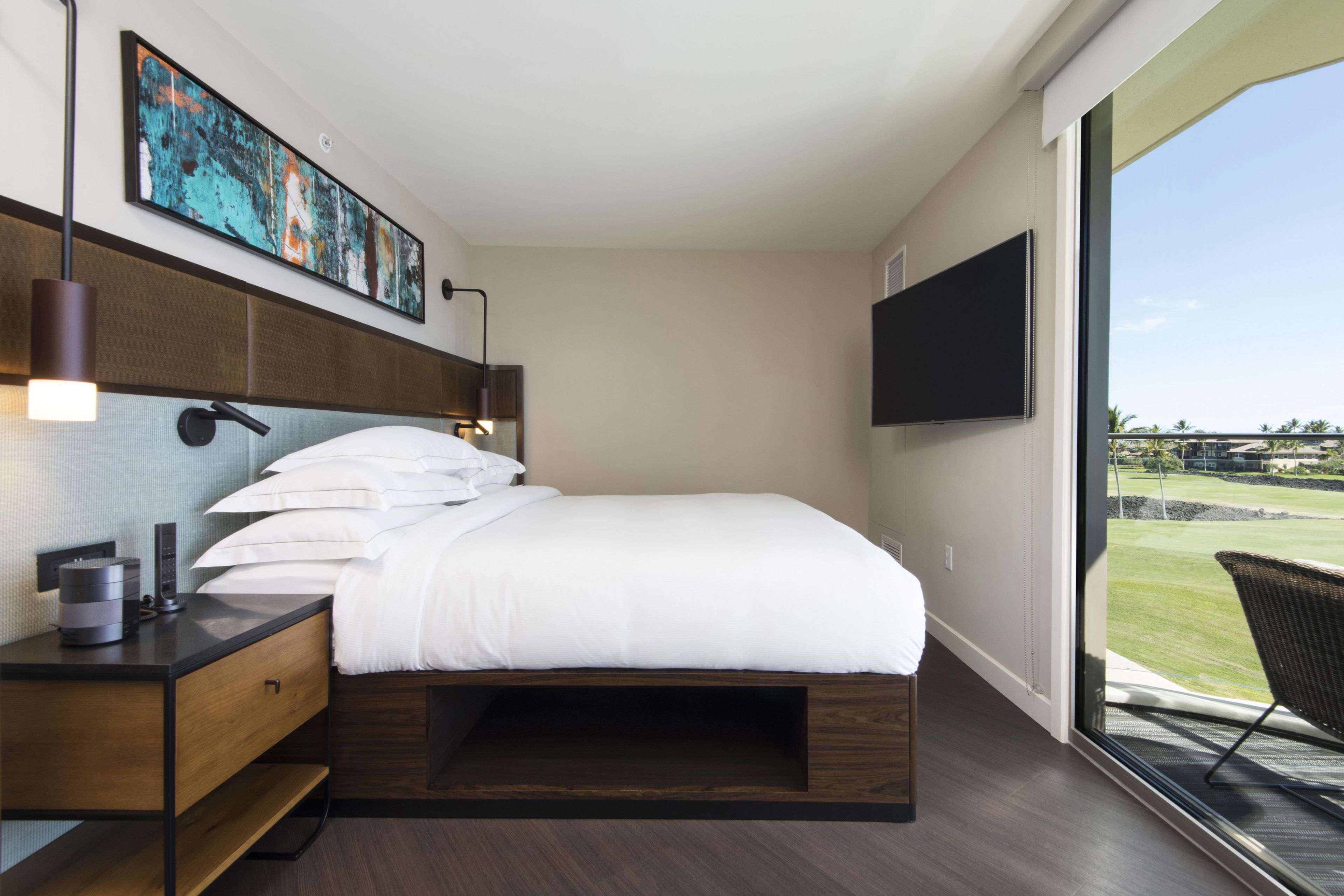 A modern hotel room with a large bed, a desk with a lamp, a flat-screen TV, and a view of a golf course.