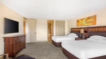 Quarto de hotel com duas camas, televisão, escrivaninha e banheiro visível por uma porta aberta.