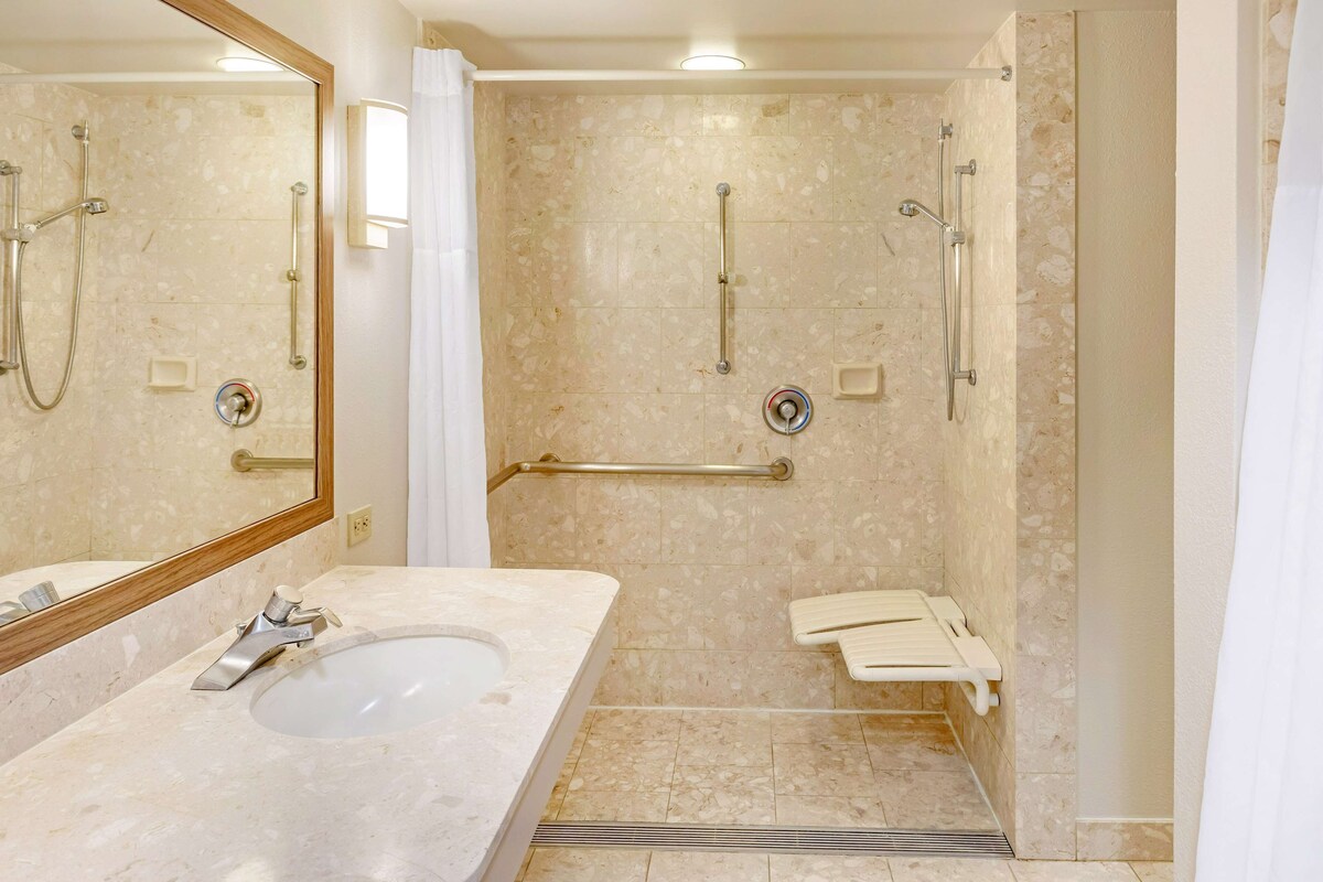 Une salle de bain équipée d’un lavabo, d’un miroir, d’une douche et de barres d’appui.