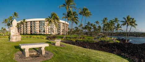A hotel with a circular building, palm trees, a statue, and a bench.