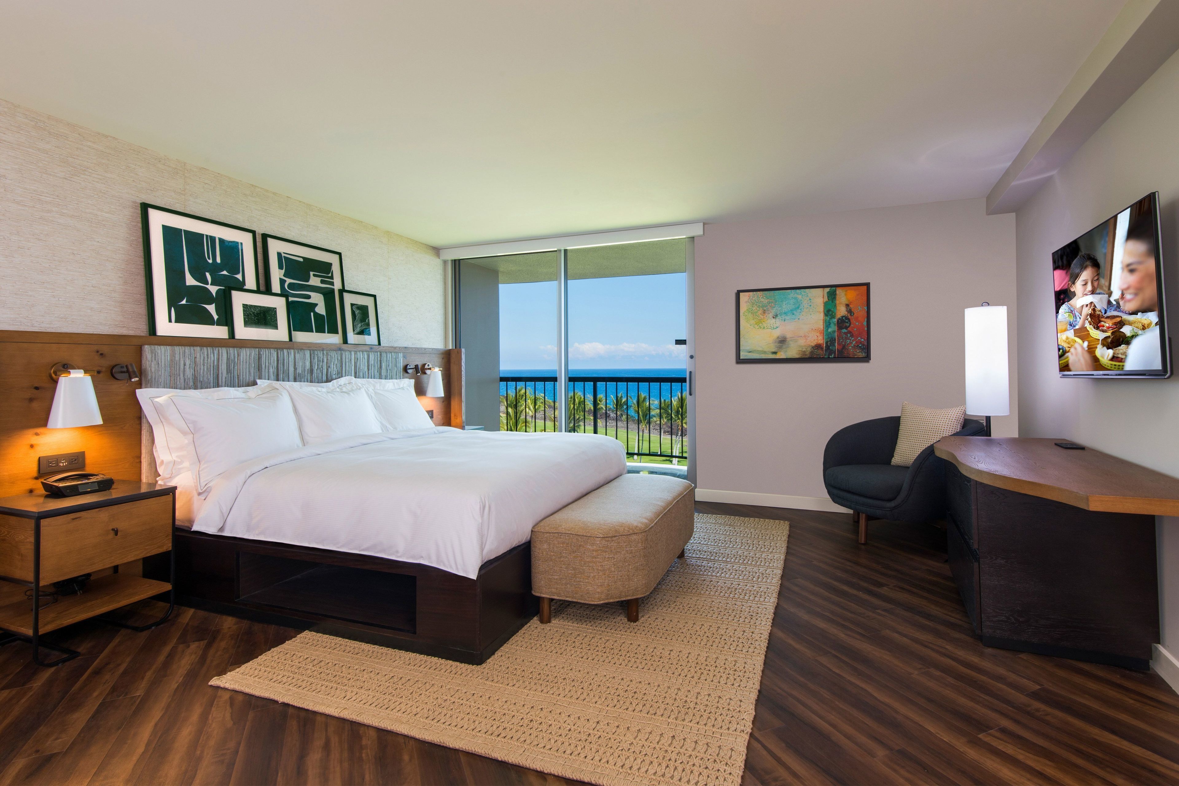 Habitación de hotel con cama, escritorio, silla, televisión y balcón con vistas.