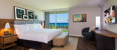 Habitación de hotel con cama, escritorio, silla, televisión y balcón con vistas.