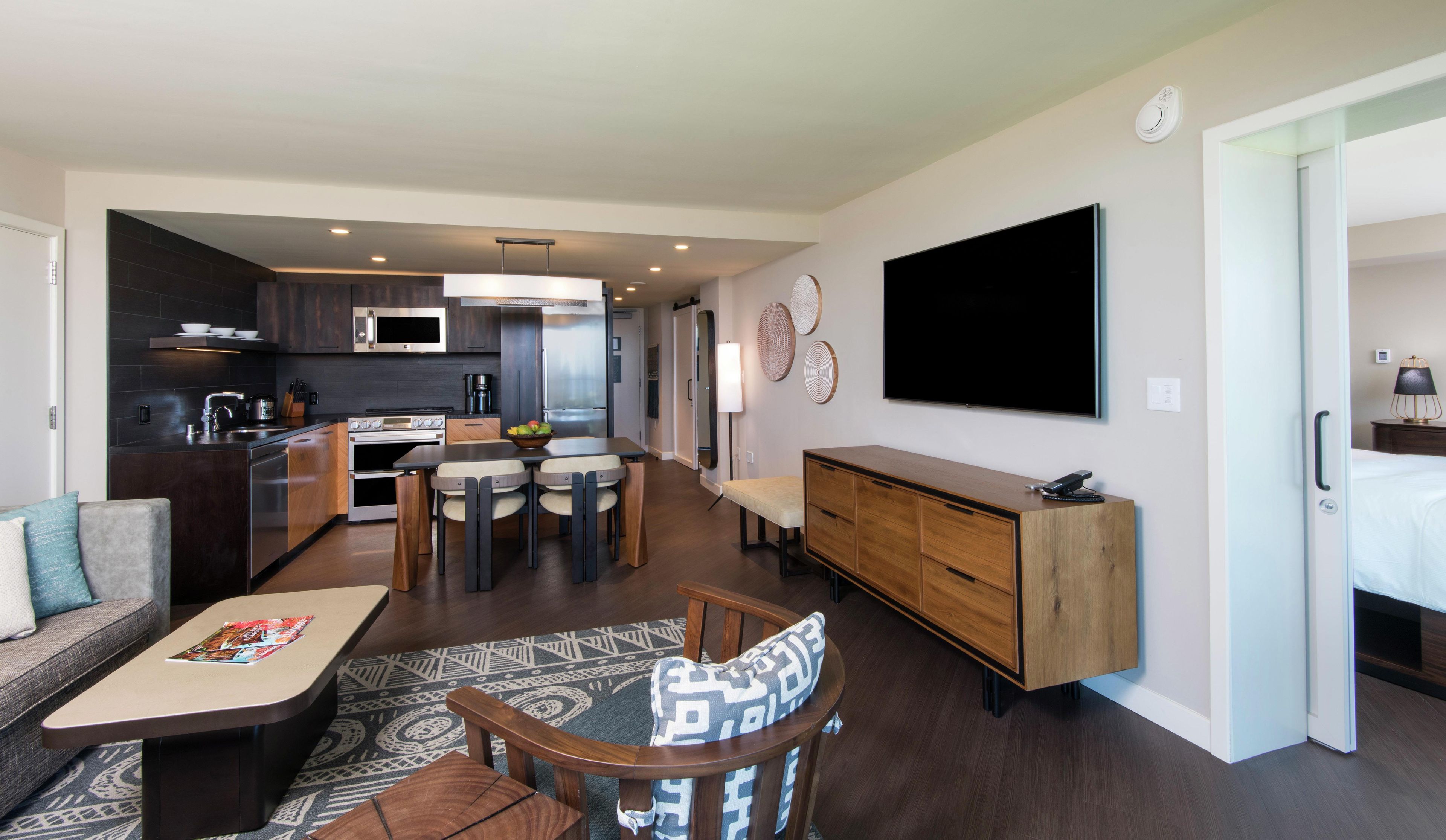 A modern living space with a kitchen, dining area, and a large flat-screen TV mounted on the wall.