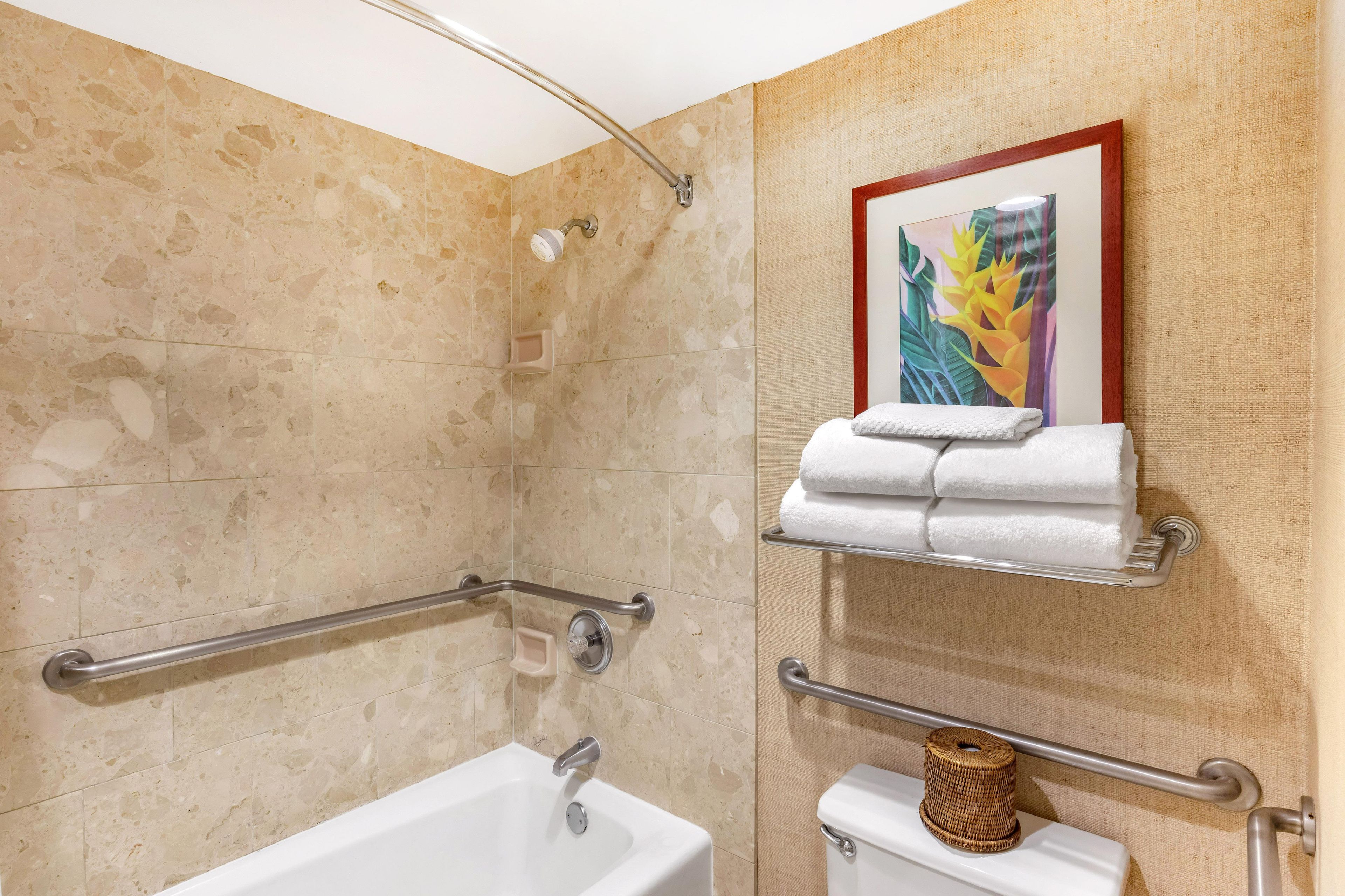 A bathroom with a bathtub, a toilet, and a shower with a handrail. There is a towel rack with towels and a framed picture on the wall.