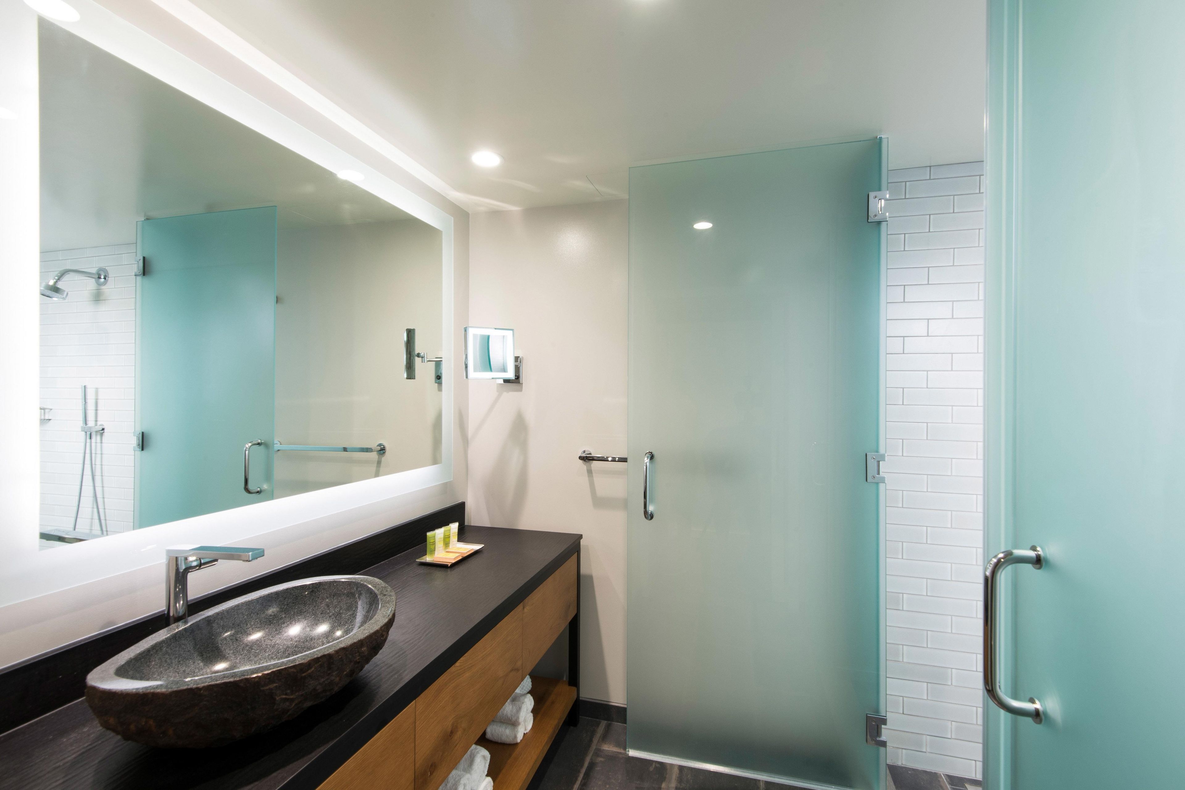 Un baño moderno con un espejo grande, un lavabo de piedra y una cabina de ducha de vidrio.