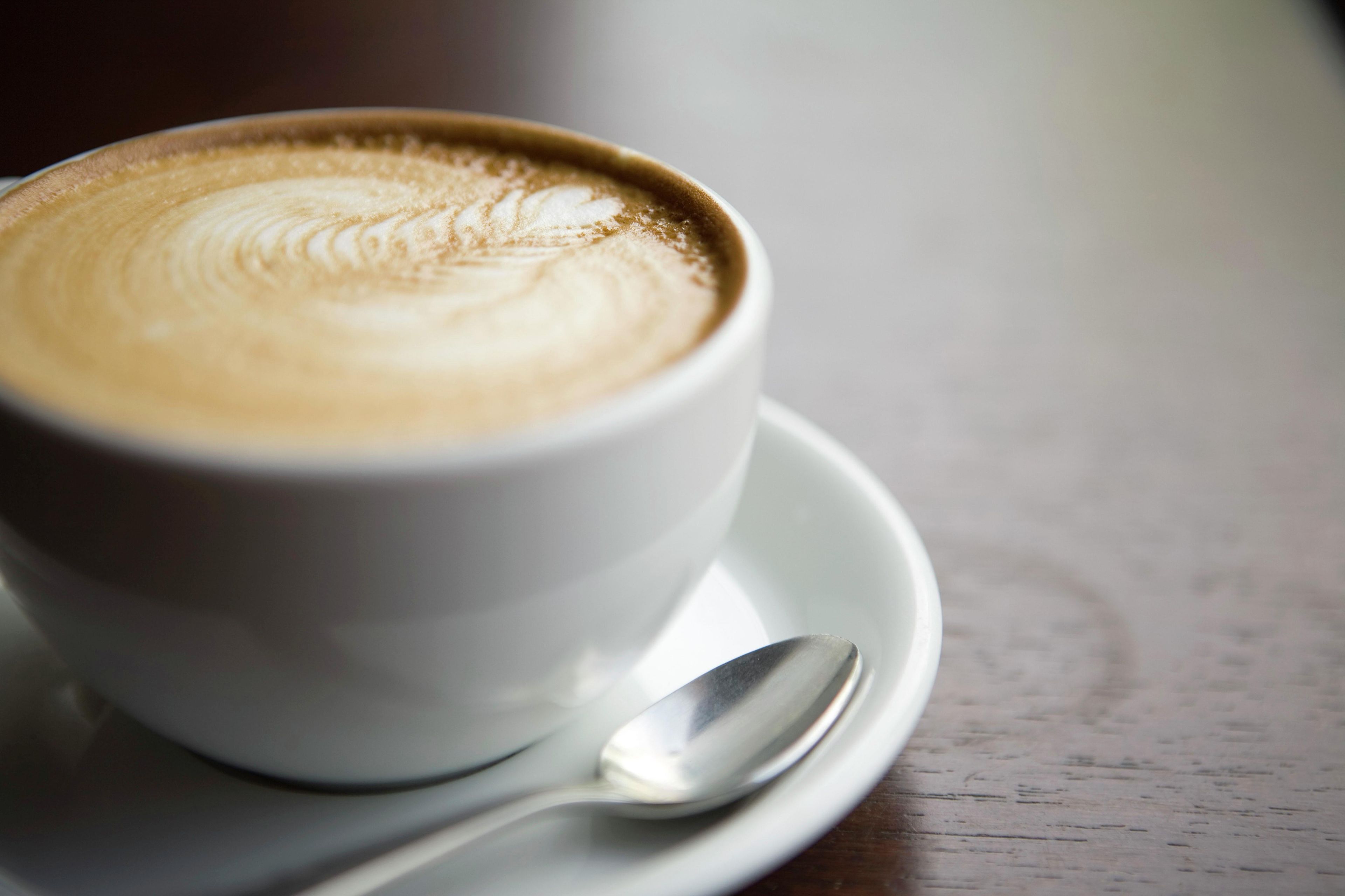 A cup of coffee with latte art on a saucer and a spoon beside it.