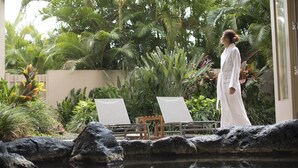 A person in a white robe standing by a pool with lounge chairs and tropical plants in the background. - Hilton Grand Vacations Club Ocean Tower Waikoloa Village (Waikoloa)