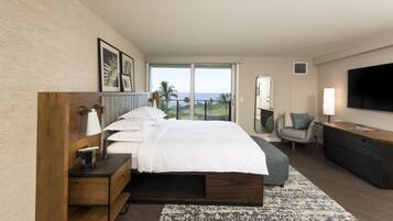 Habitación de hotel moderna con una cama grande, un escritorio, una silla, un televisor y un balcón con vistas.