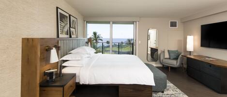 A modern hotel room with a large bed, a desk, a chair, a TV, and a balcony with a view.