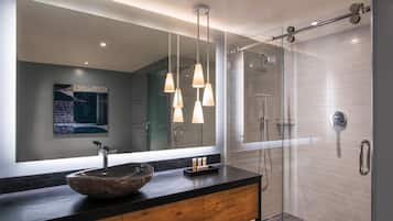 Un baño moderno con un espejo grande, un lavabo de piedra y una ducha con mampara de cristal.